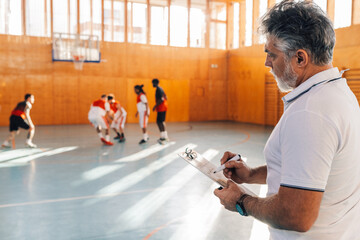 Mature basketball coach holding coach clipboard and drawing game tactic