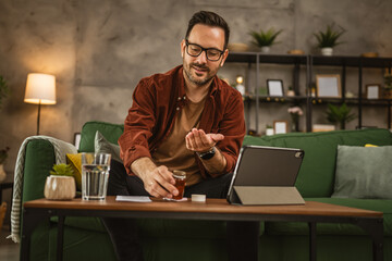 Adult man sit on sofa and prepare to drink medical pills at home