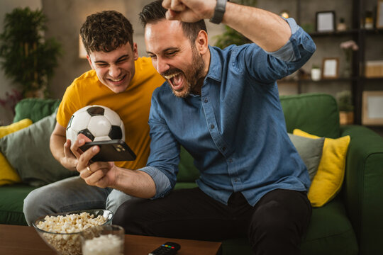 Two excited men friends brother use phone to watch football match home