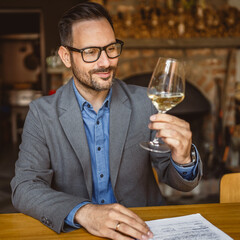 Adult man sit in a winery and hold glass of wine and clipboard