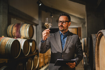Adult winemaker stand between barrels check wine quality