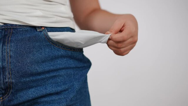 Close-up. An unrecognizable woman in blue jeans turns out her lined pocket, showing to the camera that it is empty, while dancing in place indoors against a white background