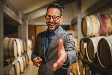 Portrait of happy adult winemaker stand between barrels in the cellar