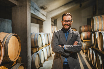 Portrait of happy adult winemaker stand between barrels in the cellar