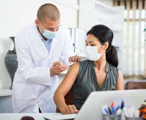 Asian female office employee in protective face mask getting antiviral injection at workplace....