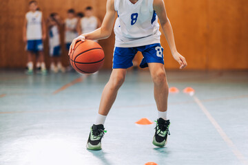 Cropped picture of junior basketball player dribbling a ball at court.