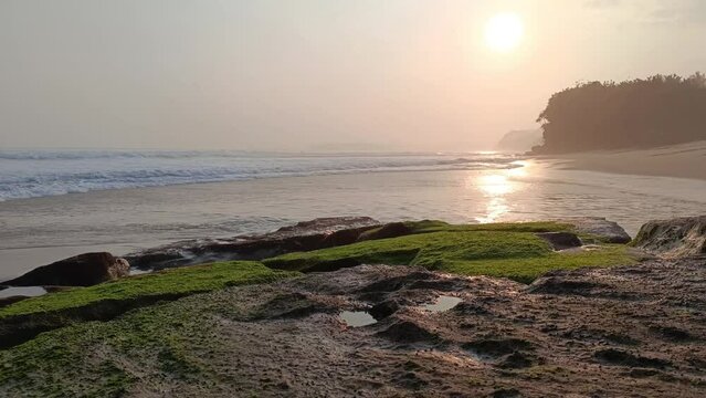 Sunset over sea waves washing the beach sand. Aerial sun setting over mountain silhouette. Tropical natural sea view on Molang beach, Indonesia