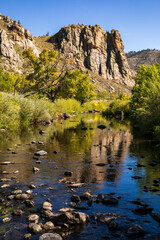 Cache la Poudre canyon as it approaches Fort Collins, CO.  Huge rock bluff, blue sky and trees.  Rocky background.  Scenic area with blue sky, rocky mountain, green bushes and trees