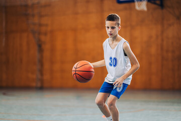 Naklejka premium Junior basketball player dribbling a ball at court on training.