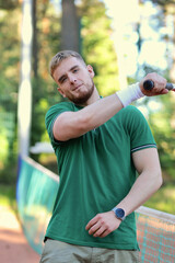 Fototapeta premium Young happy handsome man in polo play tennis outdoors with tennis racket on court at summer day