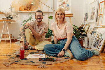 Portrait of happy artists sit on atelier floor and smiling at the camera