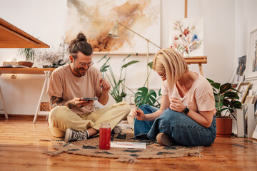Happy hipster artistic couple sitting on atelier floor and painting.
