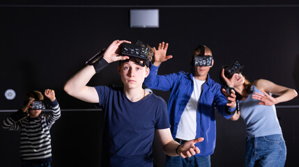 Portrait of emotional surprised teenage boy wearing VR headset playing virtual reality games with his parents and little brother