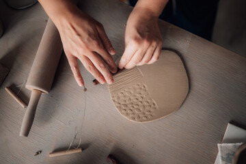 Top view of hands using decorative little rolling pin on wet clay.