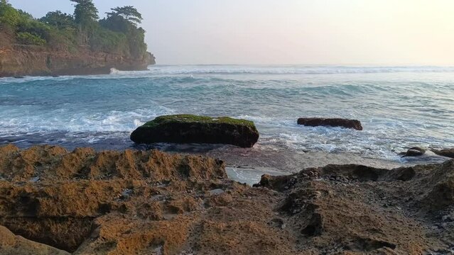 Sunset over sea waves washing the beach sand. Aerial sun setting over mountain silhouette. Tropical natural sea view on Molang beach, Indonesia