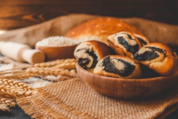 Wooden board with tasty cut poppy seed bun on table