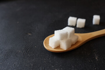 White crystalline sugar cubes on a wooden spoon