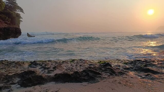 Sunset over sea waves washing the beach sand. Aerial sun setting over mountain silhouette. Tropical natural sea view on Molang beach, Indonesia