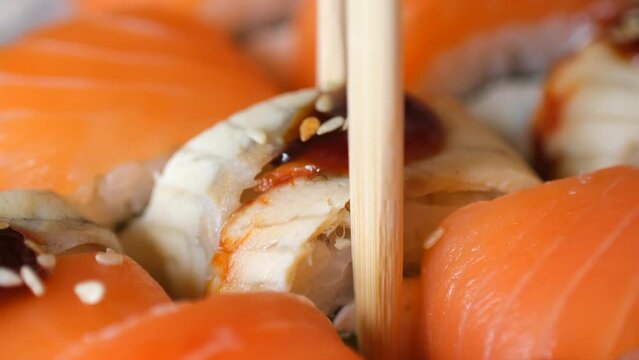 Hand hold chopsticks with sushi roll macro. Eel rolls in sushi set close up. Traditional Japanese food. Japanese kitchen with seafood. Taking one sushi roll from set using sticks for sushi.