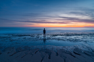 Anonymous person admiring serene sunrise on Atlanterra Beach with solitary figure