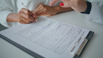Closeup patient writing form in healthcare clinic. Woman hand pointing document