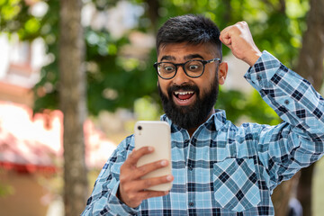 Indian bearded man use mobile smartphone celebrating win good message news, lottery casino jackpot...