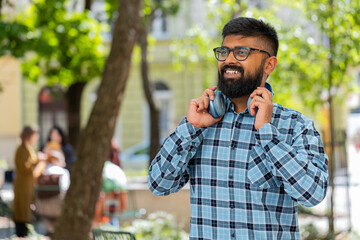 Portrait of happy smiling Indian bearded man listening music taking off headphones looking at...