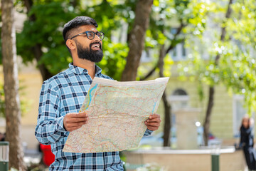 Indian young man tourist exploring city street, sightseeing holding paper map, check direction searching way looking for the route outdoors. Travel concept. Hispanic guy. Town lifestyles. Horizontal