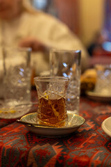 A glass of tea sits on a saucer on a table