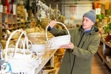 European man selecting wicker basket in salesroom of home goods store.