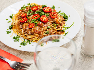 A plate of spaghetti with meat sauce and tomatoes. The plate is on a wooden table. The dish looks delicious and inviting. Italian style meal made with high quality product.