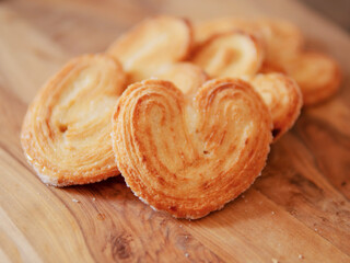 Delicate cookies made in heart shape are arranged in a stack with wooden board underneath. French style pastry sweet desert. Bakery product. Selective focus. Warm color.