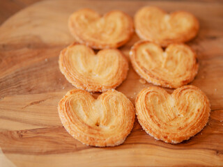 Delicate cookies made in heart shape on wooden board underneath. French style pastry sweet desert. Bakery product. Selective focus. Warm color. Tasty treat for tea or coffee