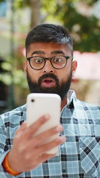 Oh my God Wow. Excited happy joyful winner Indian bearded man use smartphone celebrating win good message news lottery casino jackpot victory outdoors. Hispanic guy on urban city street. Vertical