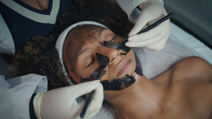 Hands applying face mask in spa salon closeup. Relaxed patient visit cosmetician