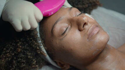 Hands rubbing face cream with brush closeup. Beautician massage african american