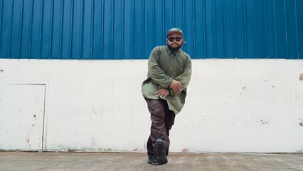 Hipster dancing b-boy foot step at street with blue wall. Asian break dancer practice street dance...