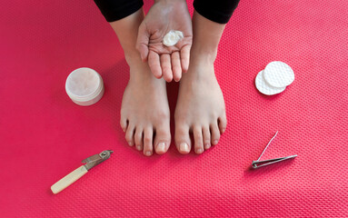 Mano de mujer joven con porción de crema hidratante para aplicar sobre los pies apoyados en un mat...