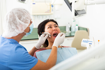 Professional dentist man examining asian female patient teeth with dental tools - mirror and probe