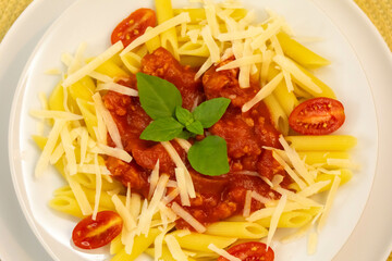 Traditional penne pasta with tomato sauce and grated cheese decorated with basil and tomatoes.