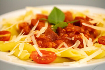 Traditional penne pasta with tomato sauce and grated cheese decorated with basil and tomatoes.