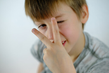 close-up face embarrassed child, happy boy 8-10 years old screwed up his eyes, victoria sign,...