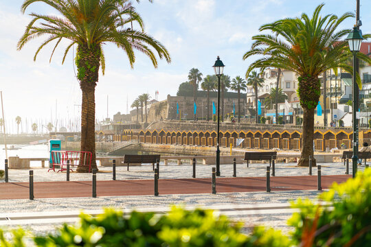 View from the boardwalk promenade at the Praia da Ribeira beach of Cascais Bay and the ancient fortress citadel, along the coast of Cascais, Portugal, Portuguese Riviera.