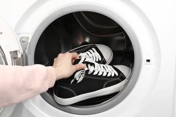 Woman putting stylish sneakers into washing machine, closeup