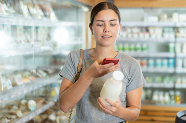 Young woman in supermarket scan QR code on bottle of milk. Girl buyer photo information on...