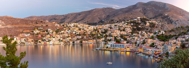 Panoramic view of Symi Island harbor with colorful houses and boats at dusk, Greece