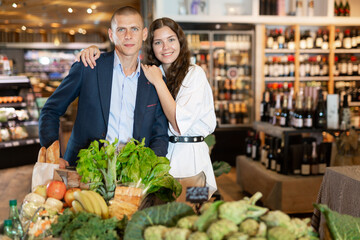 Adult couple is standing with cart with products in the supermarket