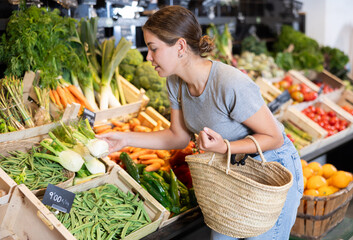 Smiling young woman customer buying fresh fennel root-crop in big grocery store