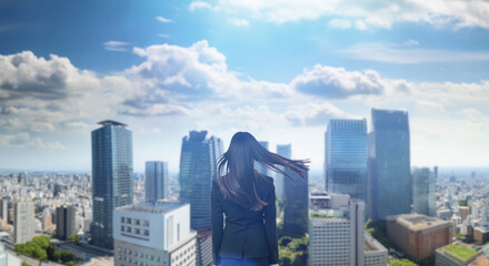 日本の街・都市・朝日を受けたオフィスビル群を前に佇み風を受けて髪をなびかせる会社員の女性の出勤　就職・ビジネス・はじまり・決意・目標・挑戦のイメージ