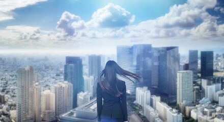 日本の街・都市・朝日を受けたオフィスビル群を前に佇み風を受けて髪をなびかせる会社員の女性の出勤　就職・ビジネス・はじまり・決意・目標・挑戦のイメージ